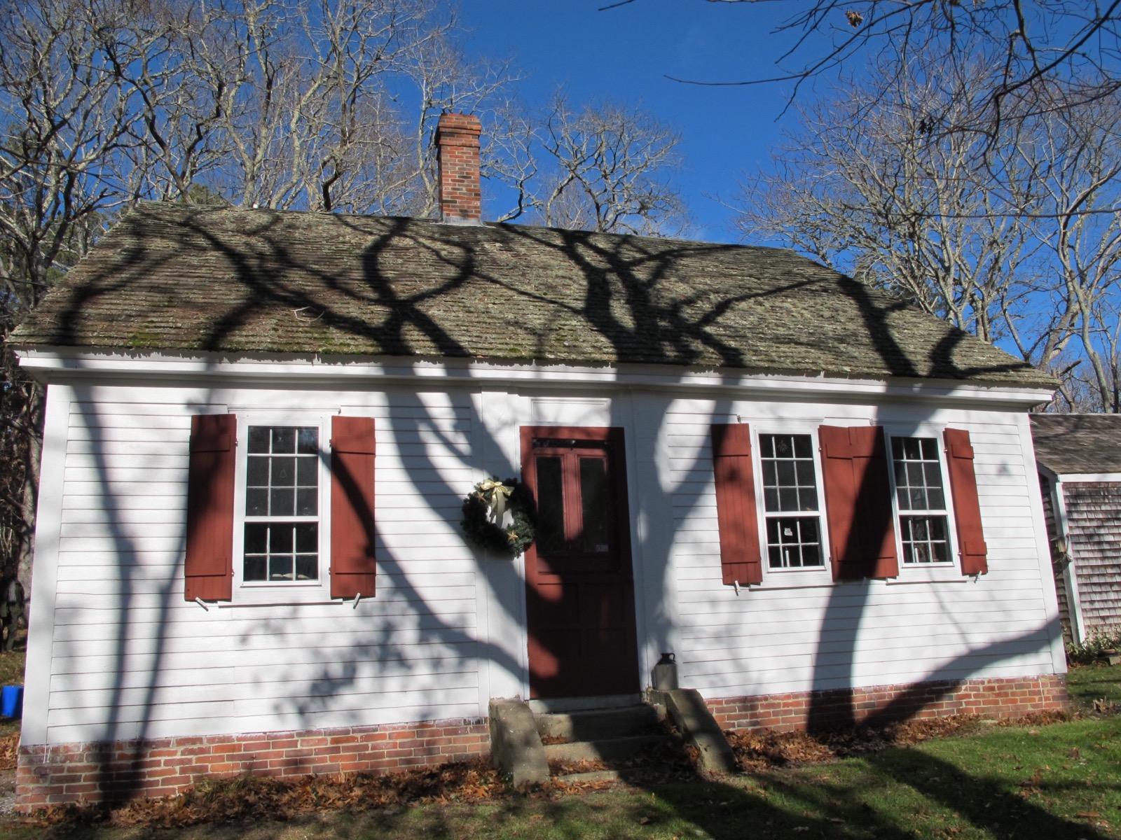 A white historic Cape Cod style house with red shutters and a brick chimney, part of Cape Cod National Seashore