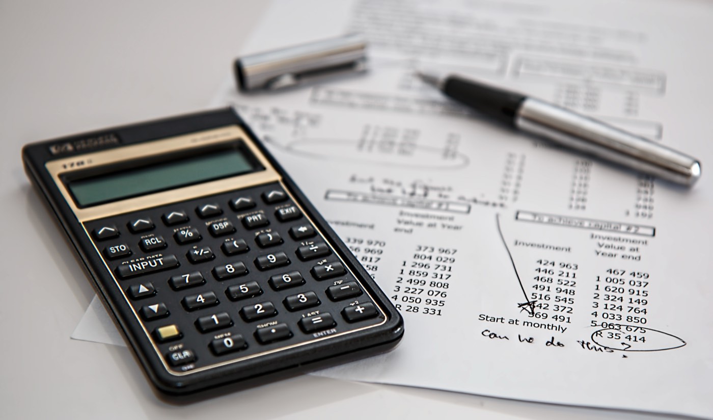 A financial calculator resting on a printed worksheet with a pen, used for planning household costs
