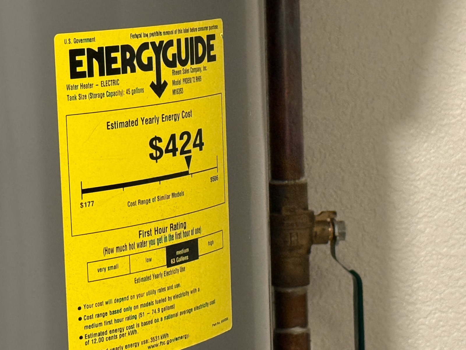 A yellow federal EnergyGuide label on an electric water heater showing its estimated yearly energy cost