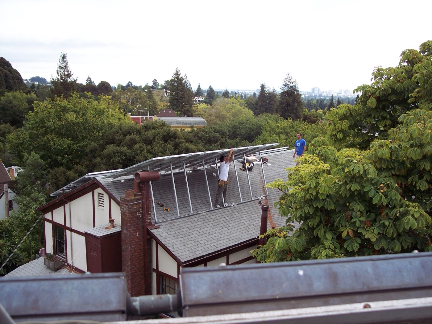 Installers crouched on a sloped residential roof closely examining solar panel mounting hardware during installation