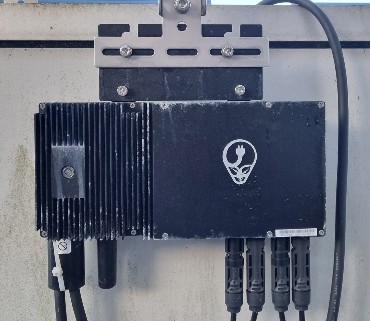 A black microinverter unit with cable connectors, the type of small electronics box installed behind an individual solar panel