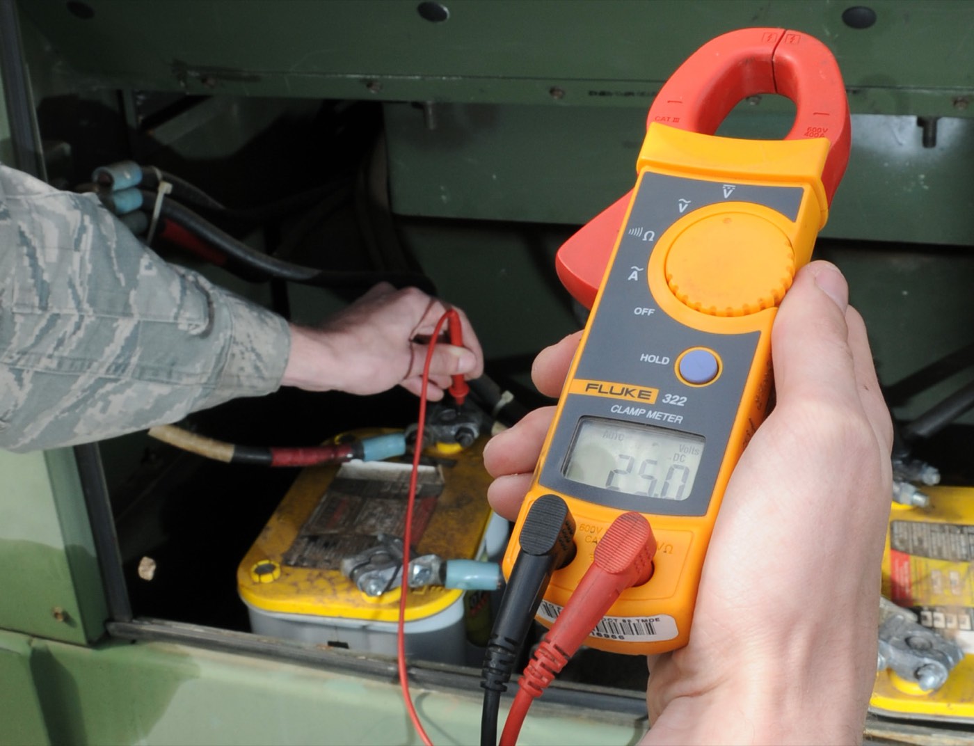 A technician holds a clamp meter while testing voltage on electrical equipment
