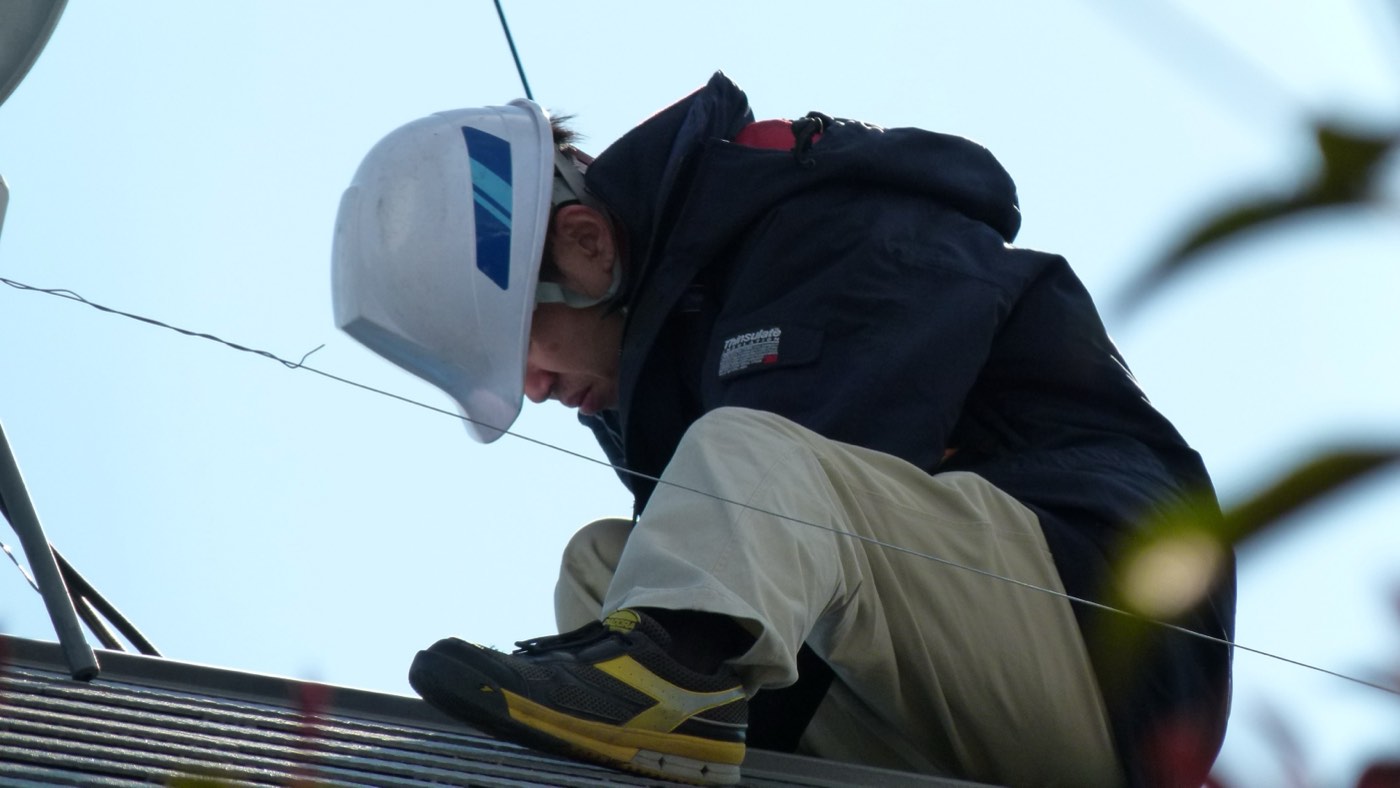 A solar installation technician actively working on a rooftop, mounting panels and hardware during installation