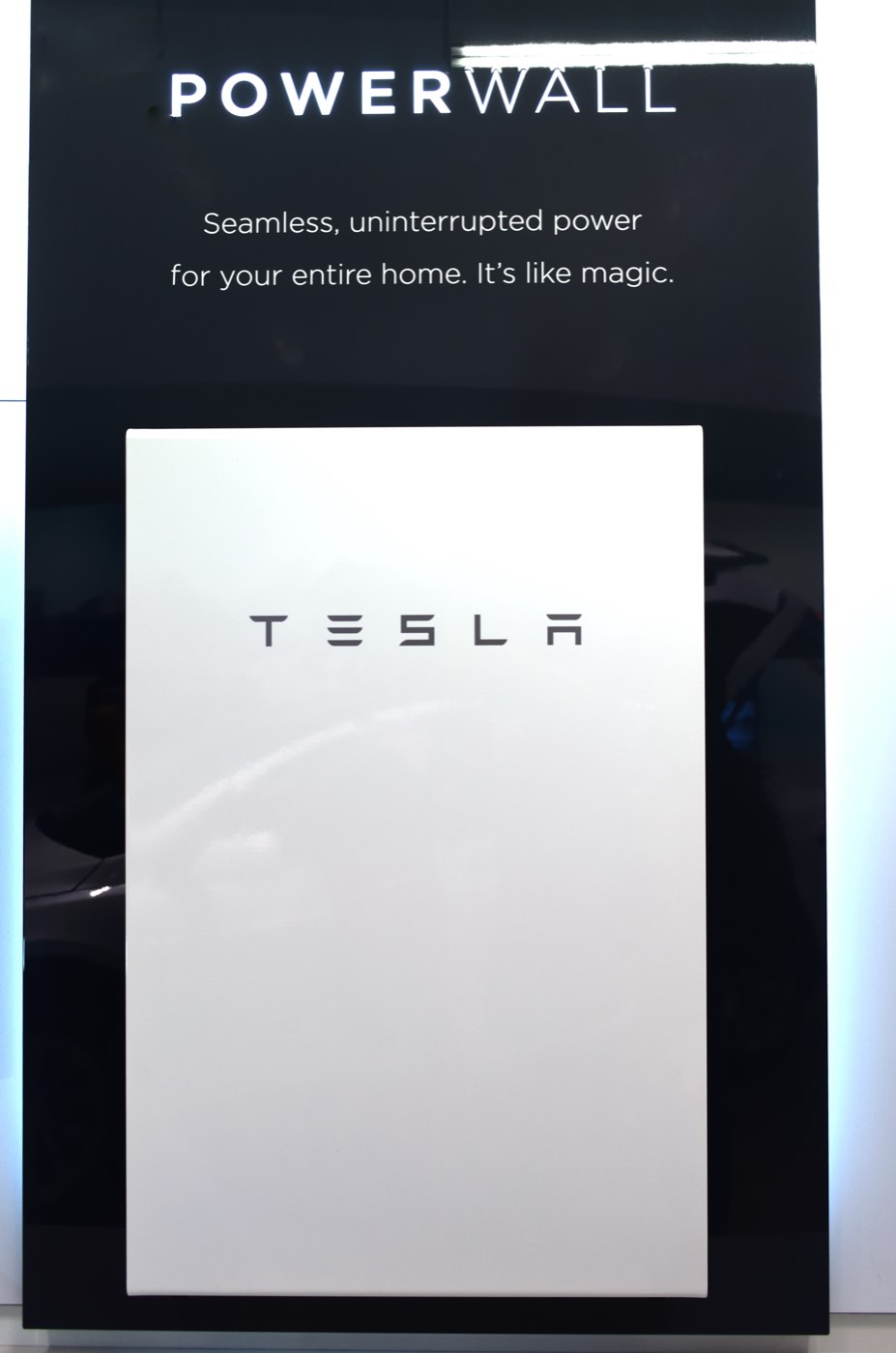 A Tesla Powerwall battery unit displayed on a showroom wall, illustrating a home battery storage product