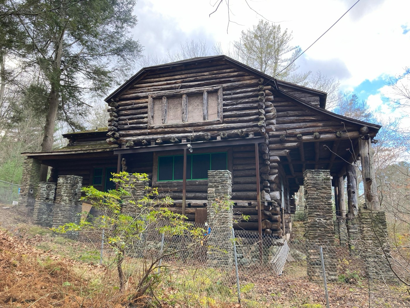 A rustic log cabin with a stone-pillared porch, surrounded by forest
